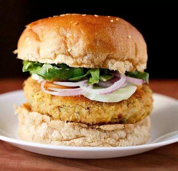 Cheesy plant-based burger featuring melted cheddar cheese, caramelized onions, and fresh greens on a brioche bun in Jaipur.